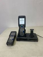 Two Intermec handheld barcode scanners on a white surface, one docked in charging station displaying boot screen