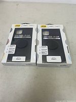 Photo of two black OtterBox Symmetry Series iPhone 11 cases with attached PopSockets in packaging on a white surface.