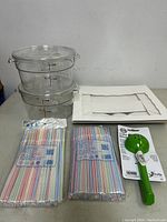 Photo of the full set showing two clear plastic bowls, two packages of colorful straws, green ladle, and white cake pan