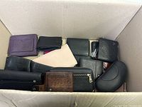 Photo showing multiple wallets and sunglass cases in a box with varied colors and materials.