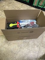 Box with contents including a yellow LED work light, assorted items in mesh bags, and covered items.