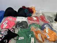 Overview of various new bras and bathing suit pieces in assorted colors, some in packaging with tags visible, laid out on flat surface.