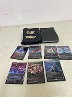 Seven Magic The Gathering Secret Lair cards spread out with two black card sleeves on a table.