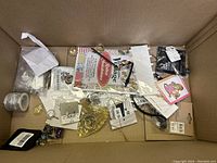 Box with assorted jewelry, cards, keychains, wire spool, and packaged items arranged inside a cardboard box.