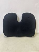 Black memory foam seat cushion pillow with ergonomic U-shaped cutout, shown removed from packaging