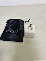 Photo of Tocara branded black drawstring pouch positioned next to a white ring display stand holding the sterling silver ring.