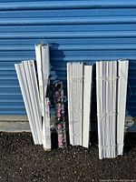 Wide shot showing multiple bundles of new white window blinds and the floral wallpaper rolls leaning against a blue background.