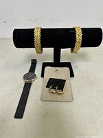 Overview of the jewelry lot showing the wristwatch, two gold-tone bracelets on black display stand, and a set of gold-tone hoop earrings on a beige display card.