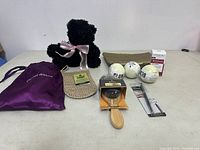 Photo showing the entire lot with all items arranged on table; includes teddy bear, loofah, bath bombs, cosmetic pouch, purple bag