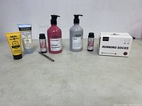 Photo showing 7 bottles and tubes of skincare, haircare, lip products, and a box of running socks aligned on a white surface against a white background.