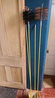 Two chimney brushes and four yellow fiberglass brush poles leaning against a wall and door.