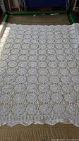 Full view of the white crocheted table cloth laid out, showing size and overall pattern.