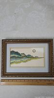 Full view of the framed watercolour painting showing the stylized mountains in blue and green tones with a gold sun on the upper right, alongside a ruler indicating image size.