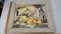 Full view of the framed oil painting with geometric cubist still life of fruits and pitcher.