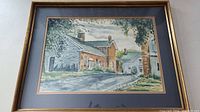 Full-framed watercolour artwork depicting a historic street with houses, mounted in a brown wooden frame with double mat.