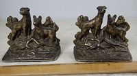 Pair of brass bookends featuring two hunting dogs standing on a log base with visible age patina and wear on the green velvet bottoms.