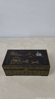 Jewelry box closed, showing top lid with hand painted scene of a horse-drawn carriage and buildings on black background with gold accents.