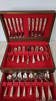 Complete set of silver plate cutlery arranged in compartments in the wooden chest with red felt lining, showing knives, forks, spoons, and other pieces.