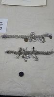 Two sterling silver charm bracelets laid flat on a surface, showing their length and attached charms.