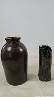 Full view of 10 inch brown stoneware crock and black handmade pottery vase side by side