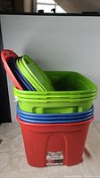 Stack of various colored storage tote lids and containers, predominantly green, blue, purple, and red plastic totes with lids.