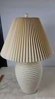 Front view of the table lamp showing the pottery base and cream pleated shade while unlit.