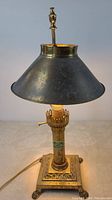 Lamp in full view showing tarnished brass base, metal shade, and finial