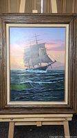 Full view of the framed oil painting showing a sailing ship at sea under a colorful sky.