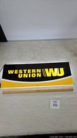 Front view of double-sided Western Union lit sign showing brand name and logo in yellow on black and yellow background with ruler for measurement.