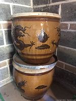 Two large ceramic garden pots stacked, showing decorative oriental dragon and claw motifs on a glossy brown glazed surface.