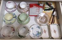 Top view of six sets of bone china teacups and saucers with floral patterns along with corkscrews, dessert plates, candy cane spreaders, and cheeseboard with utensils