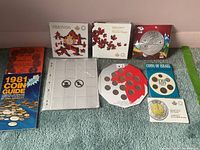 Photo of assorted collectible coins and coin guides arranged on carpet, showing various commemorative coins including Heart of Our Nation, Maple Leaves, Vancouver 2010 Winter Games, Coins of Israel, and Battle of Vimy Ridge with corresponding packaging and coin sheets.