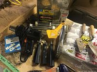 Photo showing a black heat gun, yellow scraper tool, staple gun, paint brushes, and fastener boxes.