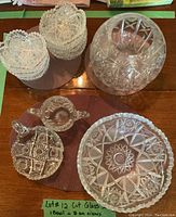 Cut glass bowls, dishes and vase with intricate star and geometric cut patterns shown on wooden table.