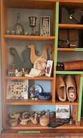 Shelf with multiple vintage decorative items including glassware, wooden chicken roosters, ceramic figurines, clock, and other small objects.