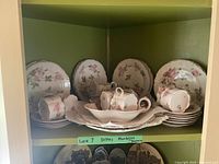 Photo showing bread plates, teacups, saucers on shelving unit with floral rose pattern and gold trim.