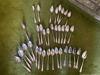 Top view showing multiple rows of collectible souvenir spoons on green surface, different sizes and handle designs.
