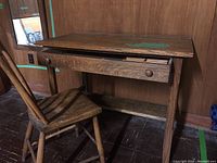 Full view of vintage wooden desk with single drawer, and matching wooden chair positioned beside it.