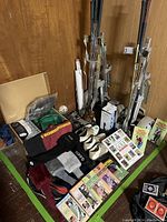 Photo shows golf clubs standing upright against the wall with golf shoes and assorted golf accessories including gloves, socks, books, and DVDs laid out on the floor.