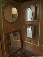 Four vintage mirrors positioned against a wood paneled wall; includes a large round mirror, a rectangular mirror, and two smaller rectangular mirrors.