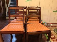 Front view of all six oak dining chairs arranged in two rows showing ladder-back design and peach patterned seats