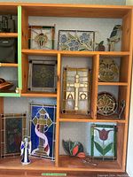 View of various stained glass panels arranged on wooden shelves showing floral, cross, and abstract designs.