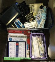 Overview of a black basket filled with various stamp collection items such as catalogs, loose stamps, tools, and organizing trays.