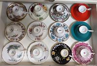 Top-down view of twelve teacups placed upside-down on matching saucers showing backstamps and patterns