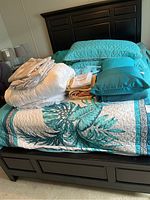 Full view of queen size bed with teal and white patterned quilt, folded sheets, teal shams, and pillows visible.