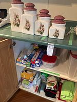 Wide view of lower kitchen cabinet shelves showing various kitchen storage items, plastic wraps, dishcloths, and cleaning supplies.
