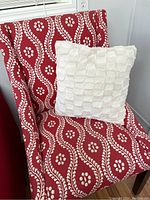 Close-up front view of one red occasional chair showing white vines and floral pattern upholstery with cream textured throw pillow on seat.