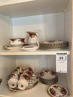 Shelf with cream pitcher, sugar bowl, serving tray, stacked plates, teacups, saucers, teaspoon holder