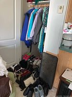 Wide view showing coats and jackets hanging, shoes and purses on floor at lower corner.