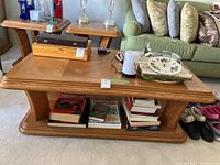 Oak coffee table with items on top and books stored on lower shelf.